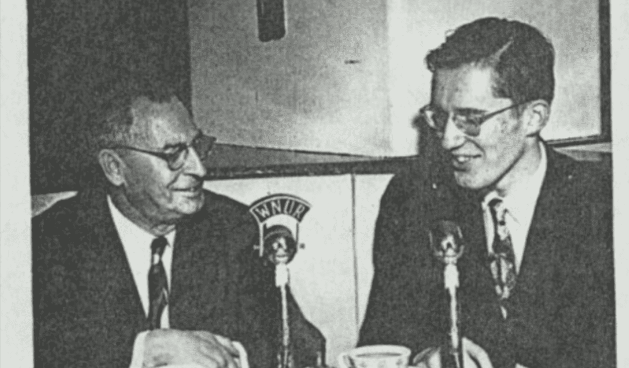 Two men talk at a microphone